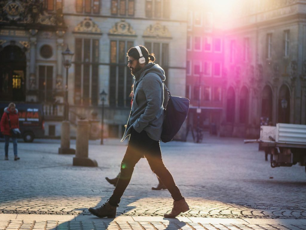 man in gray hooded jacket walking on gray bricks pavement