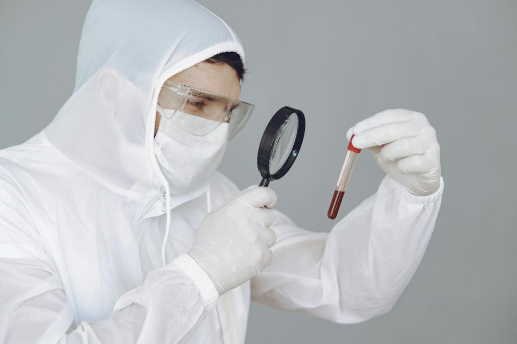 person wearing personal protective equipment while holding magnifying glass and test tube