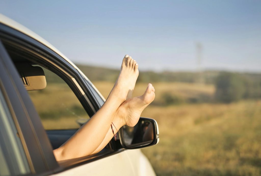 crop carefree woman with legs sticking out of car window