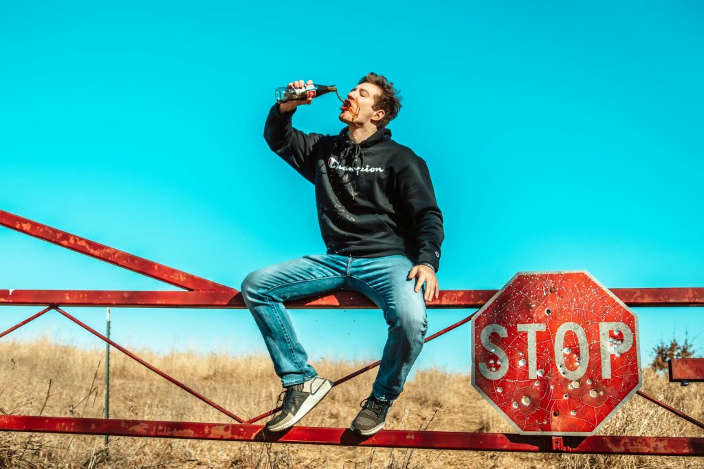 man sitting on metal fence drinking soda