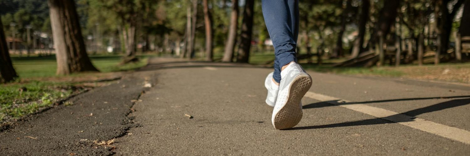 person in blue denim jeans and white sneakers walking on road