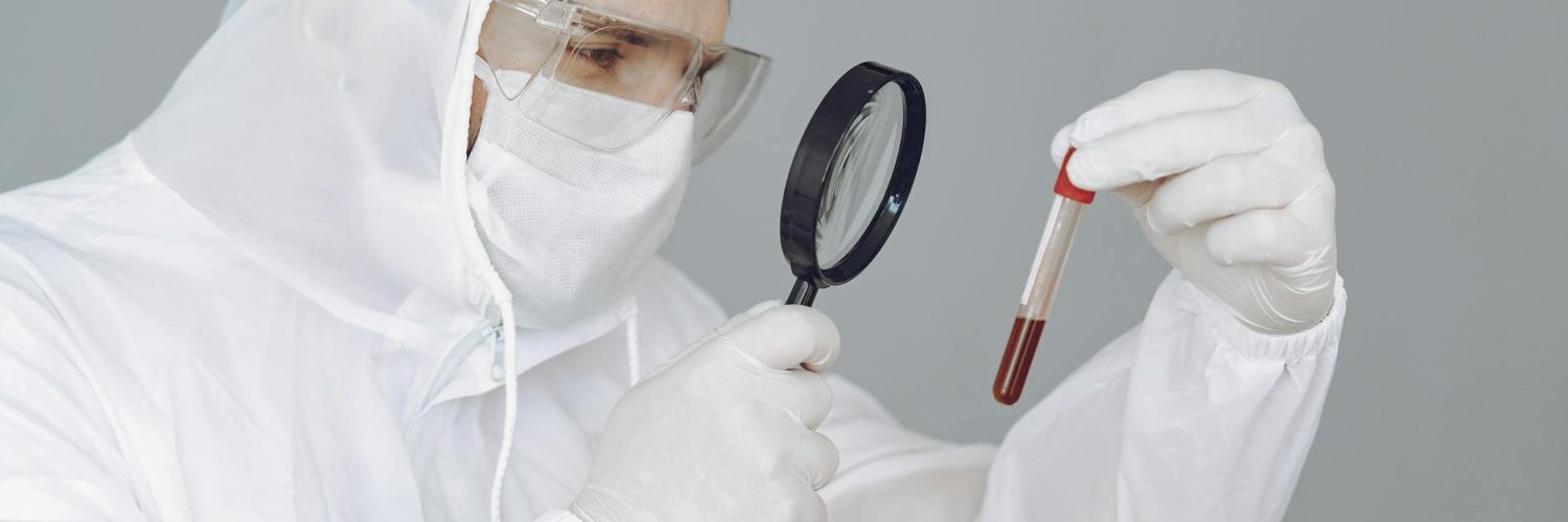 person wearing personal protective equipment while holding magnifying glass and test tube