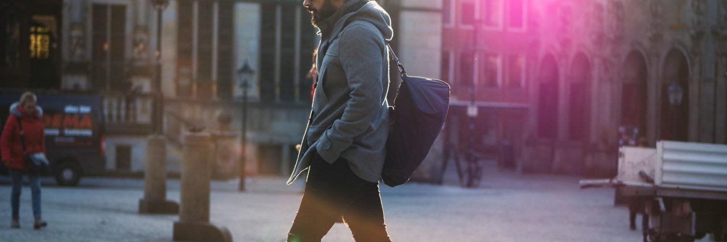 man in gray hooded jacket walking on gray bricks pavement